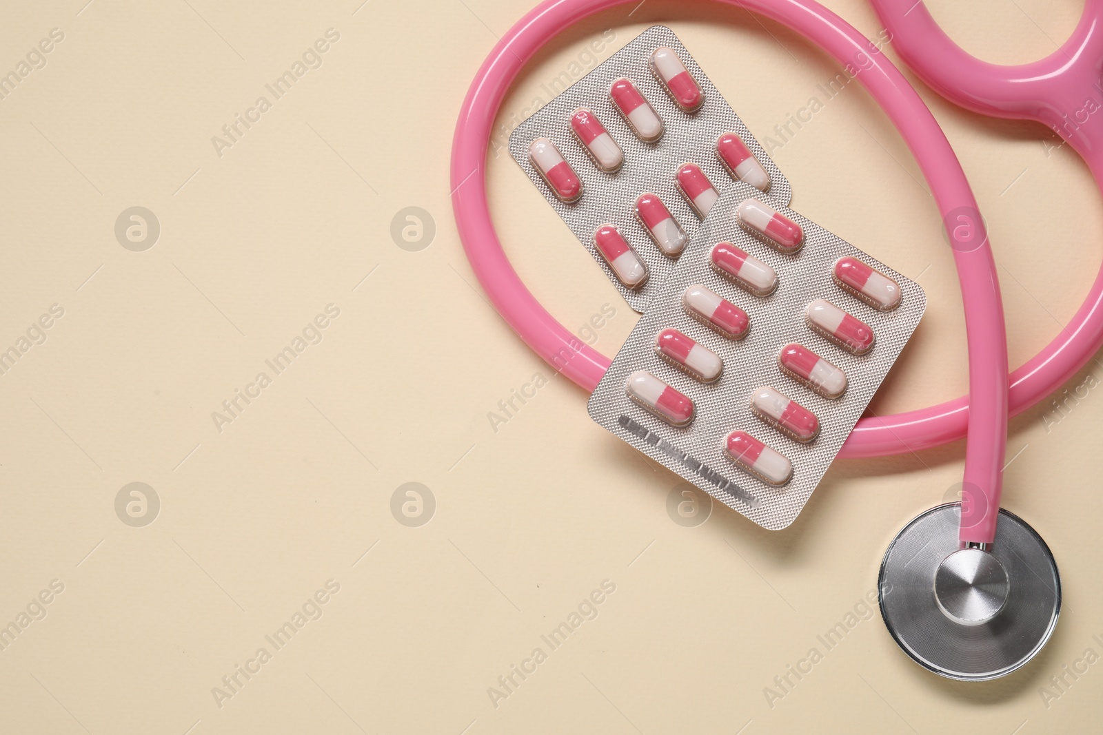 Photo of Antibiotic pills in blisters and stethoscope on beige background, flat lay. Space for text