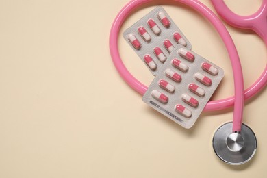 Photo of Antibiotic pills in blisters and stethoscope on beige background, flat lay. Space for text