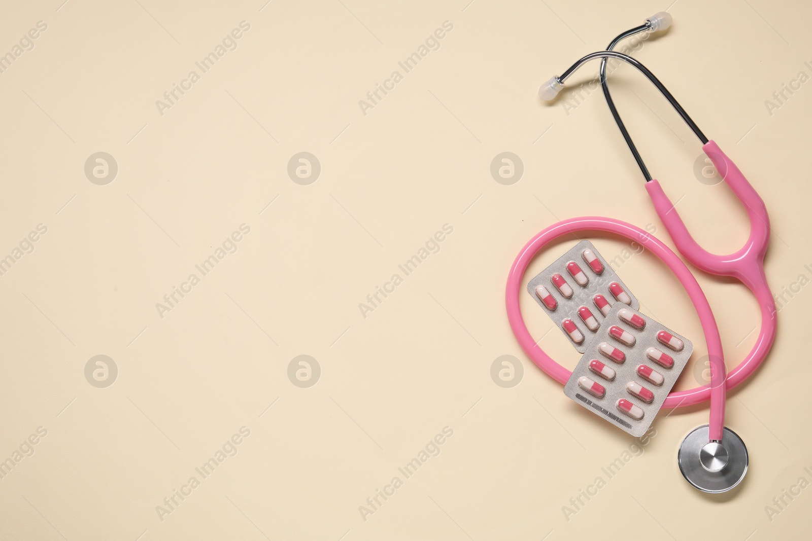 Photo of Antibiotic pills in blisters and stethoscope on beige background, flat lay. Space for text