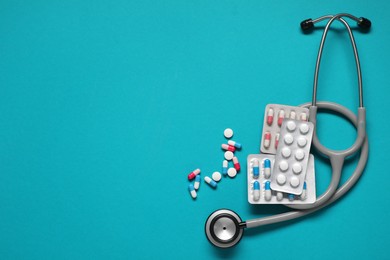 Photo of Antibiotic pills and stethoscope on light blue background, top view. Space for text