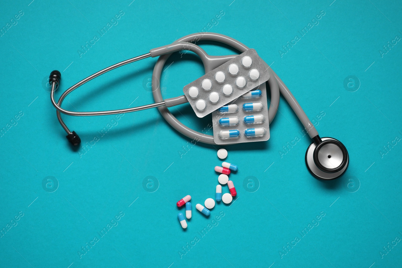 Photo of Antibiotic pills and stethoscope on light blue background, top view