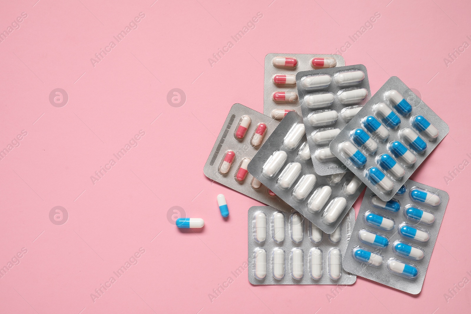 Photo of Antibiotic pills in blisters on pink background, top view. Space for text