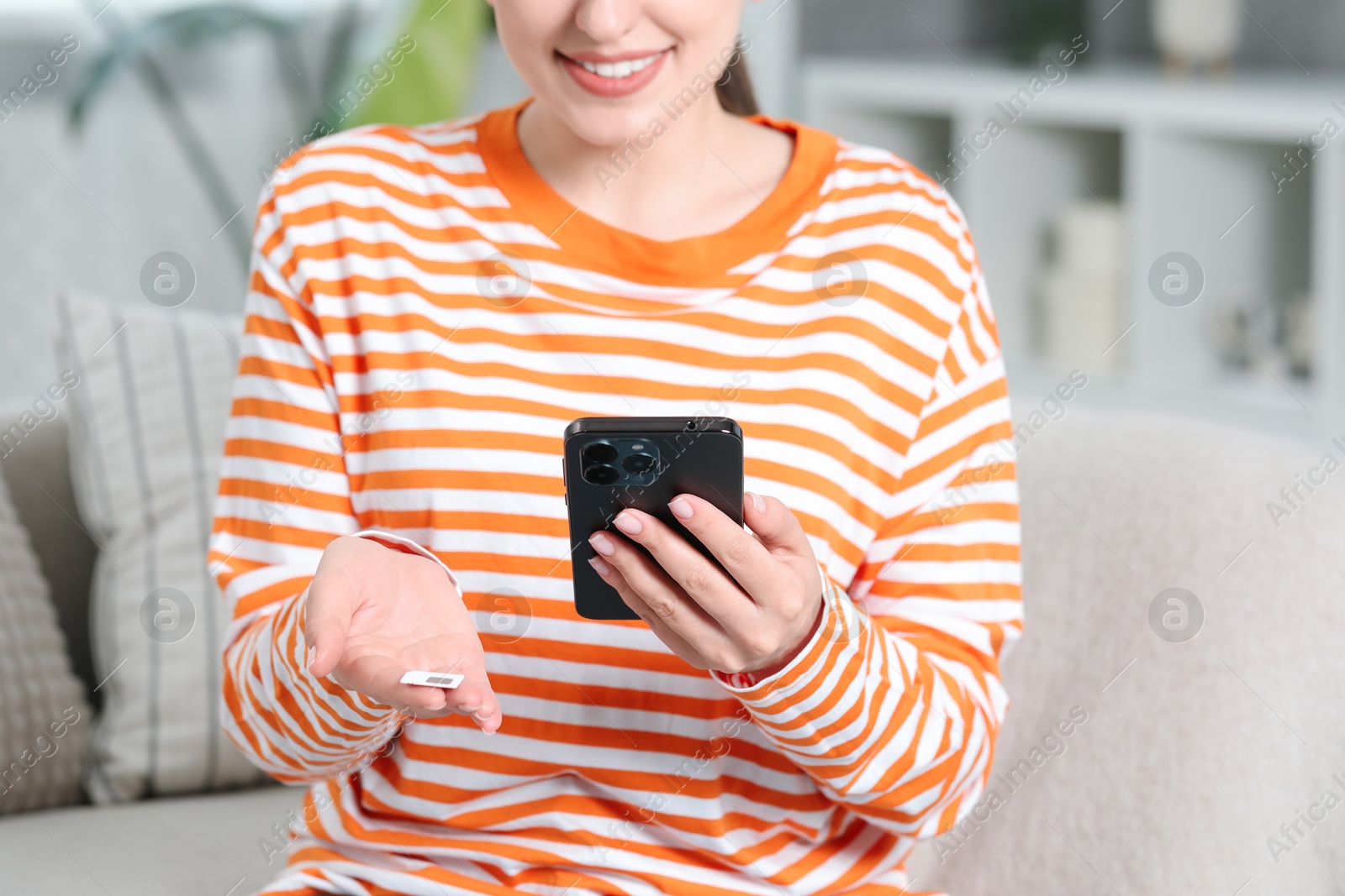 Photo of Woman holding SIM card and smartphone on sofa indoors, closeup