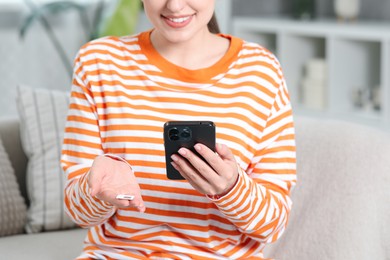 Woman holding SIM card and smartphone on sofa indoors, closeup