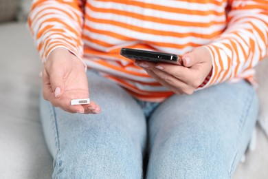 Woman holding SIM card and smartphone indoors, closeup