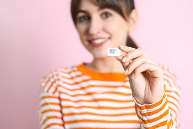 Photo of Woman holding SIM card on pink background, selective focus