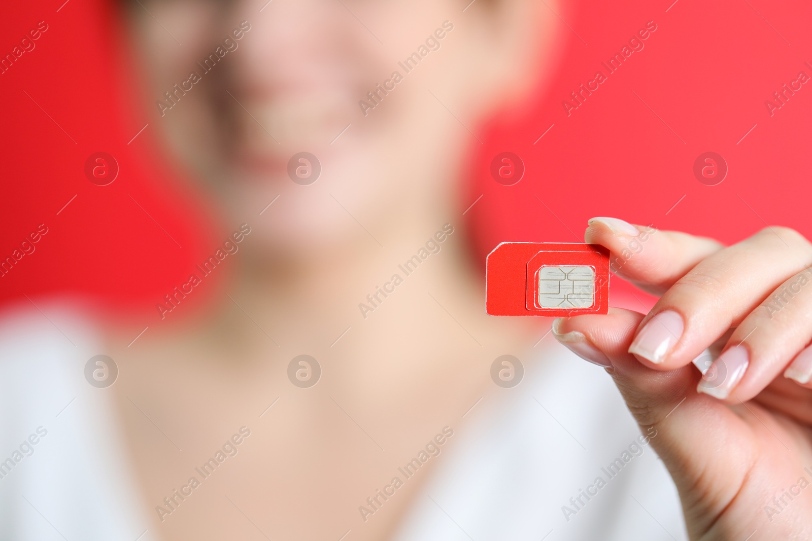 Photo of Woman holding SIM card on red background, closeup