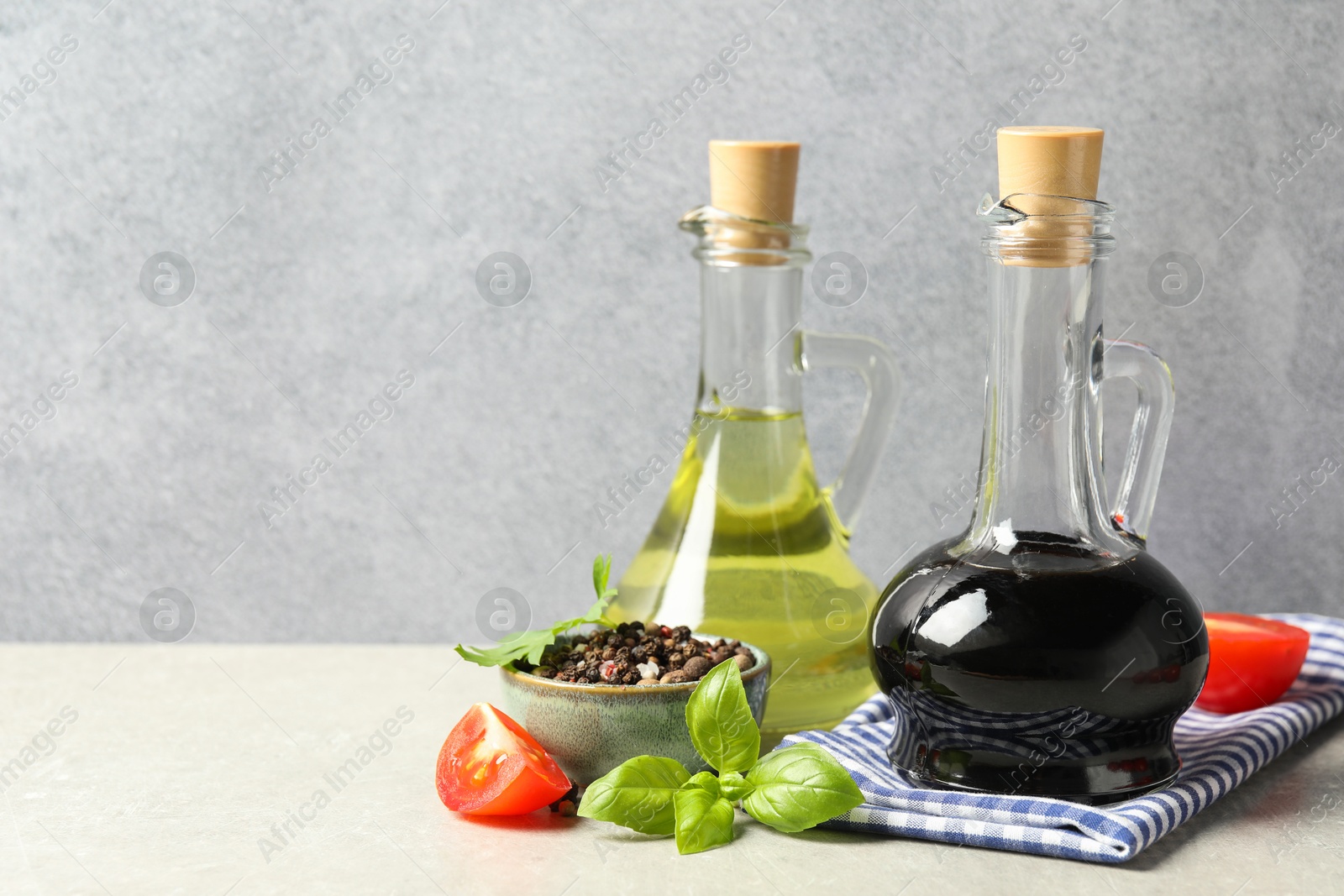 Photo of Balsamic vinegar in glass jug, oil, tomatoes, herbs and spices on gray textured table, space for text