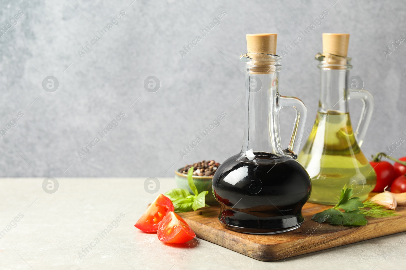 Photo of Balsamic vinegar in glass jug, oil, tomatoes, herbs and spices on gray textured table, space for text