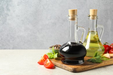 Photo of Balsamic vinegar in glass jug, oil, tomatoes, herbs and spices on gray textured table, space for text