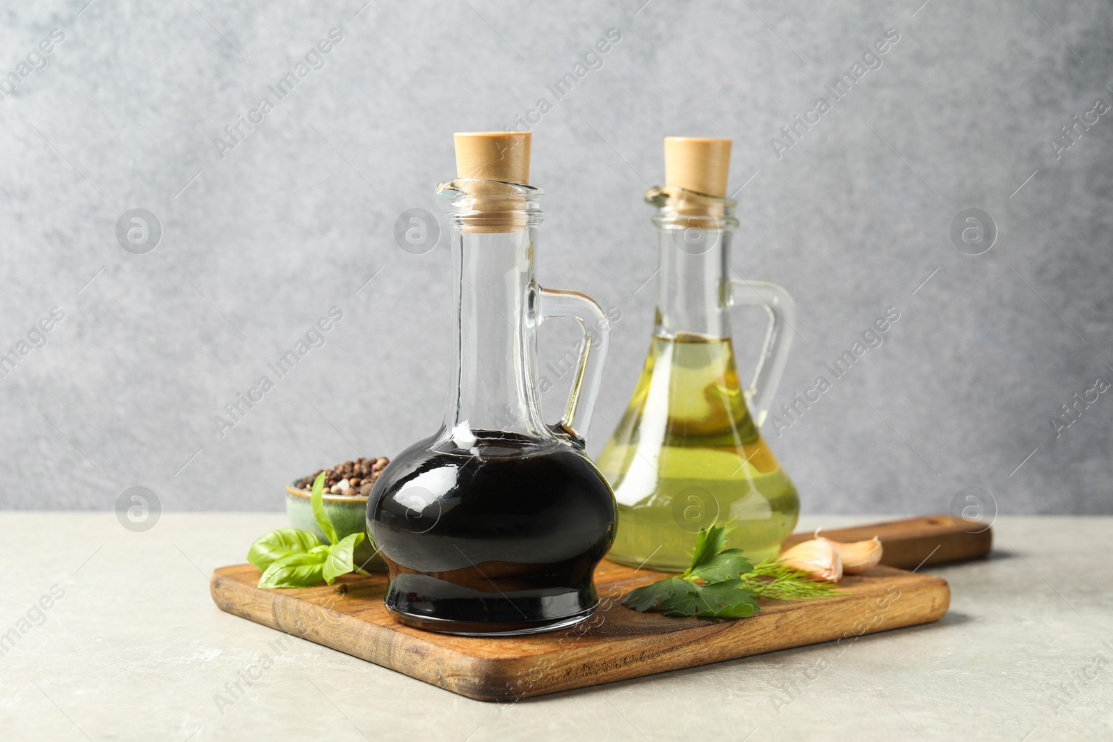 Photo of Balsamic vinegar in glass jug, oil, herbs and spices on gray textured table