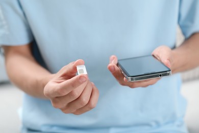 Photo of Man with SIM card and smartphone indoors, closeup