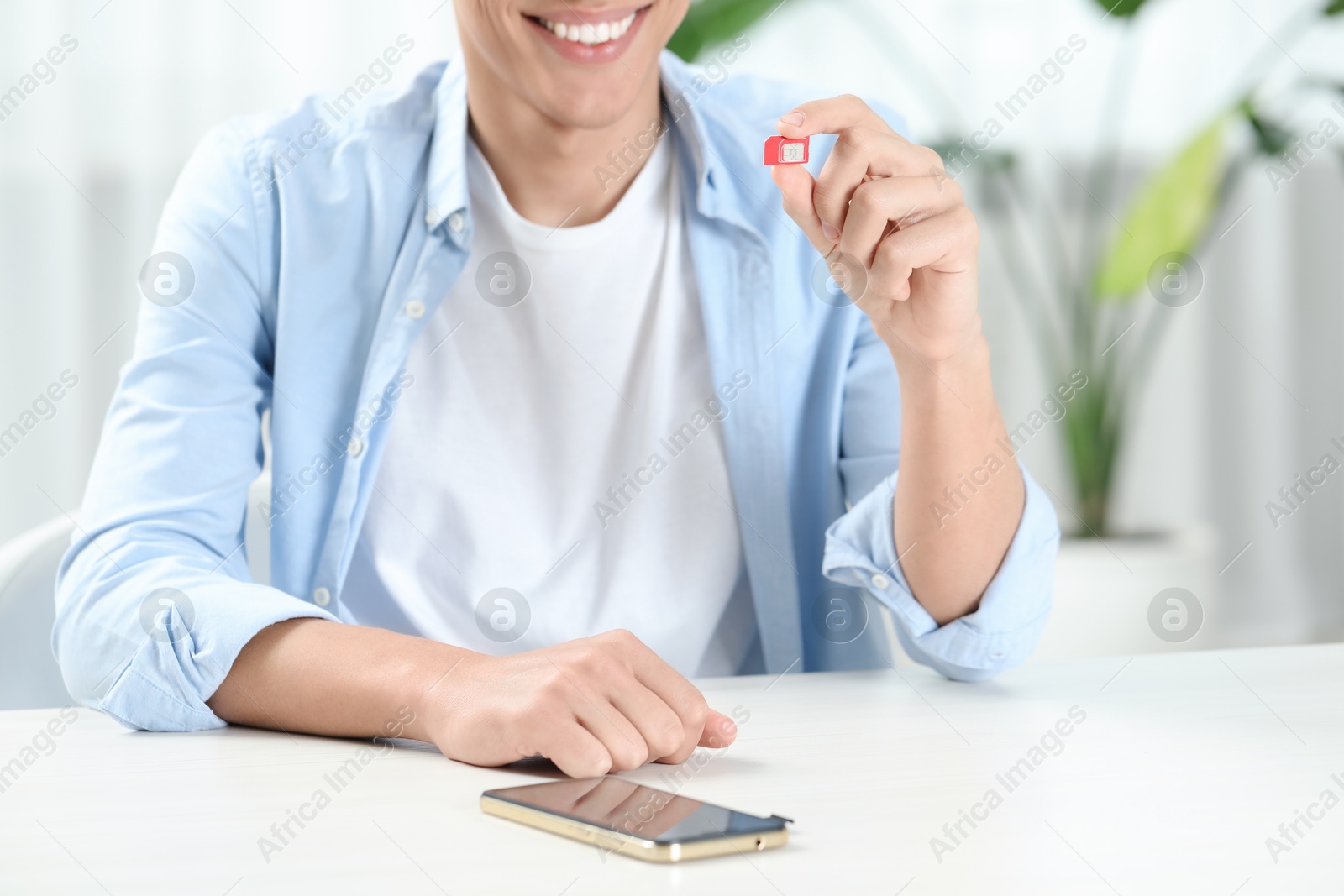 Photo of Man holding SIM card at white table with smartphone indoors, closeup