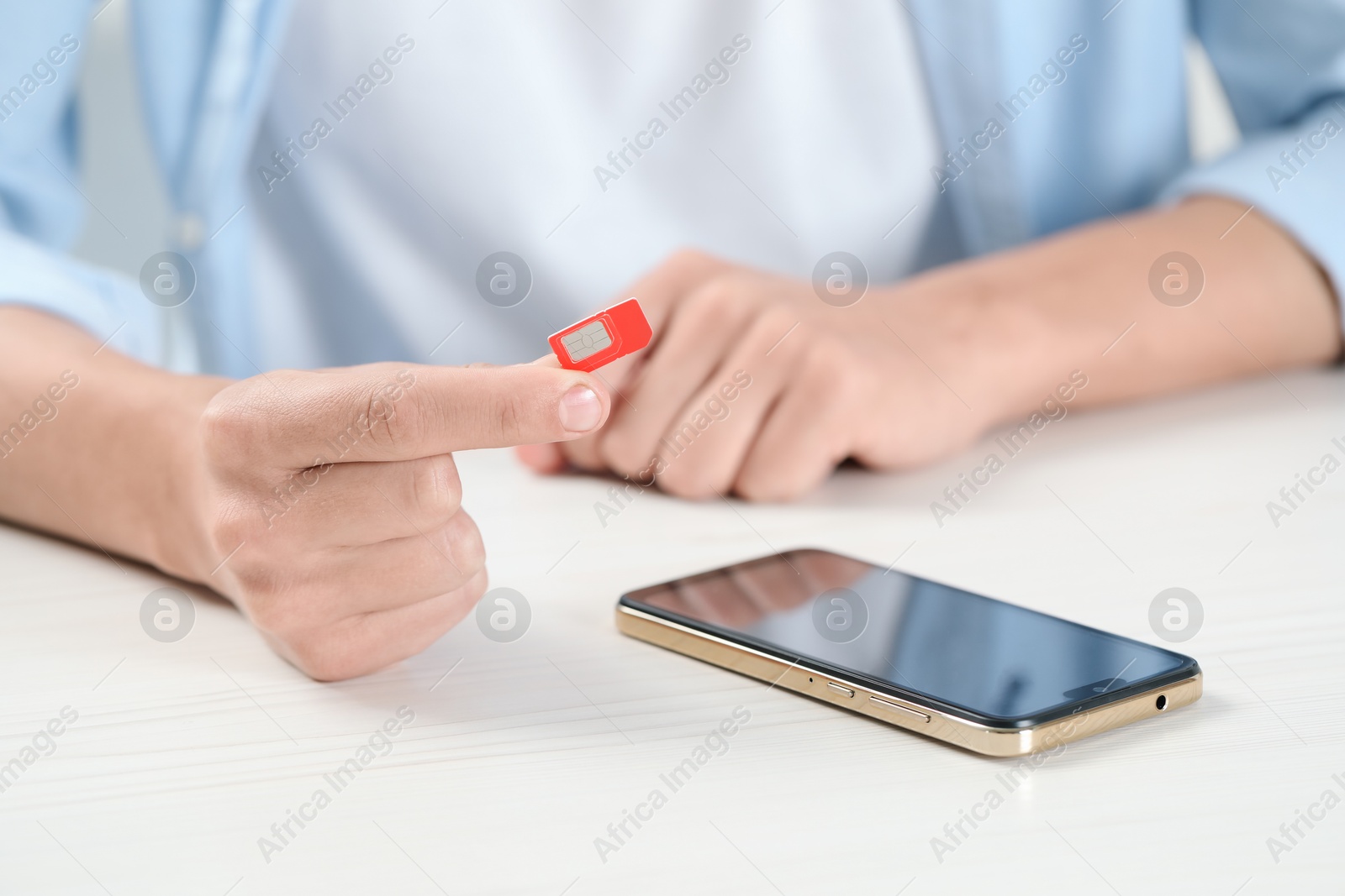 Photo of Man holding SIM card near smartphone at white wooden table, closeup