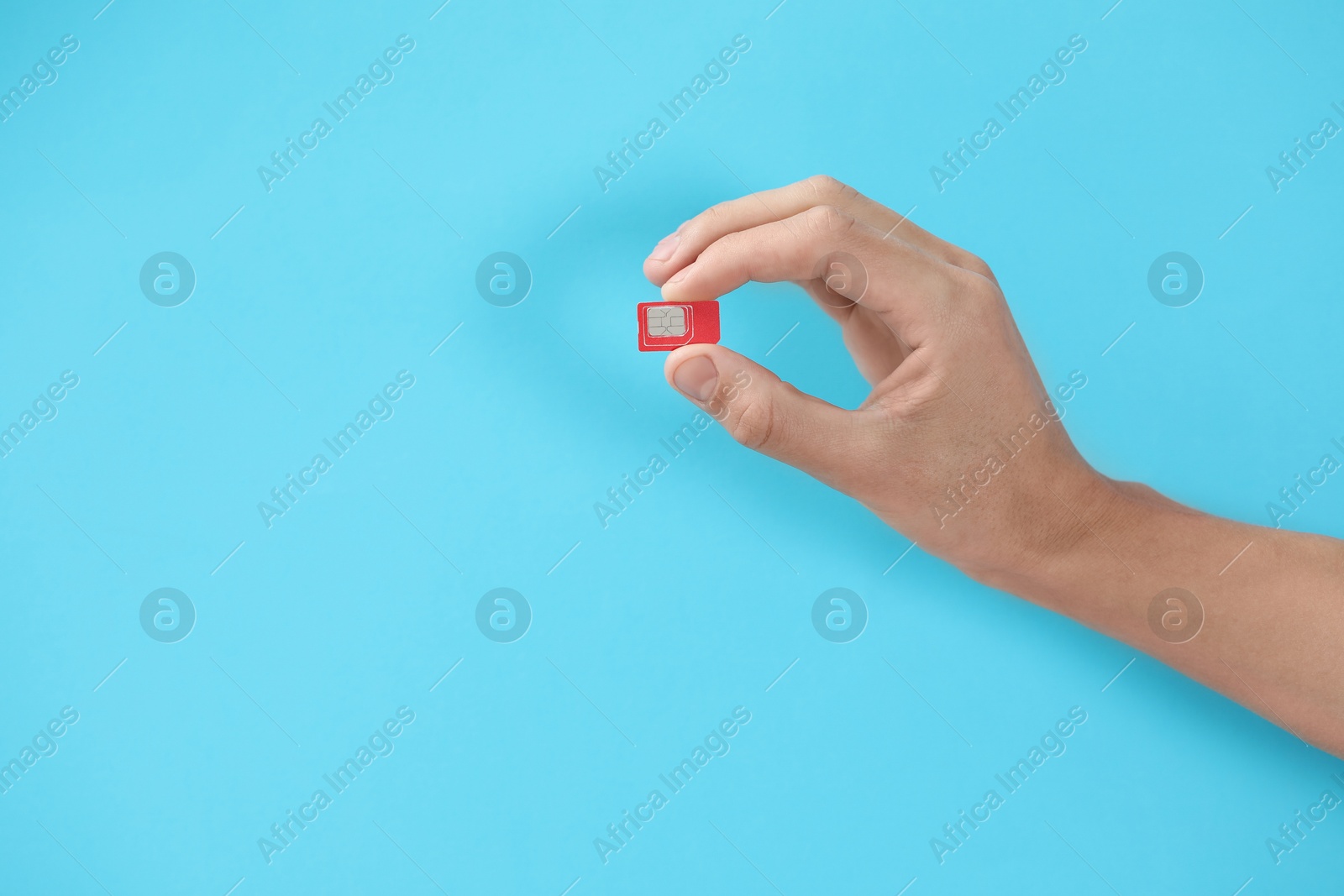 Photo of Man with SIM card on light blue background, closeup. Space for text