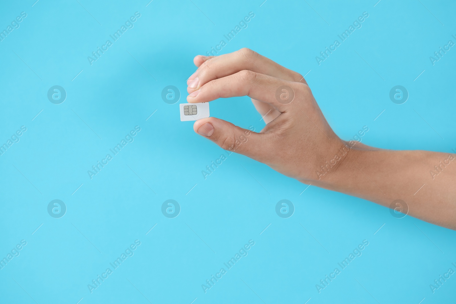 Photo of Man with SIM card on light blue background, closeup