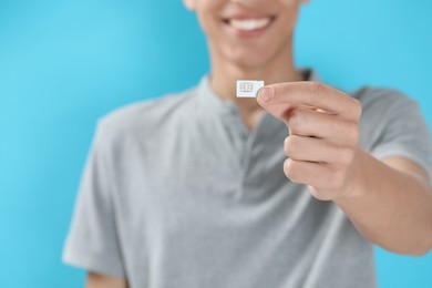 Man with SIM card on light blue background, closeup