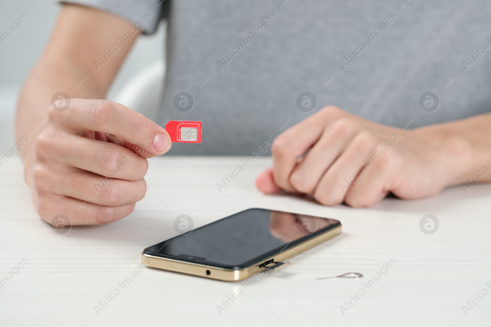 Photo of Man with SIM card near smartphone at white wooden table indoors, closeup