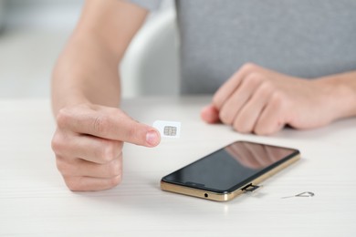 Man with SIM card near smartphone at white wooden table indoors, closeup