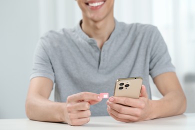 Man with SIM card and smartphone at white table indoors, closeup