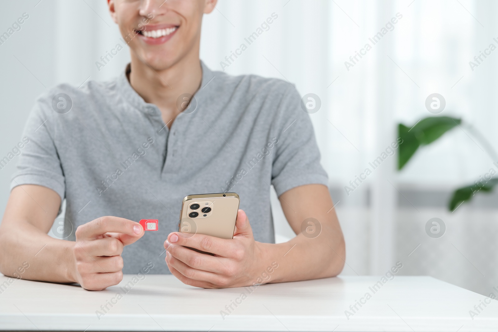 Photo of Man with SIM card and smartphone at white table indoors, closeup. Space for text