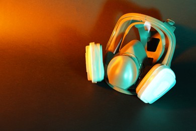 Photo of One respirator mask on dark background in orange light, top view and space for text. Safety equipment