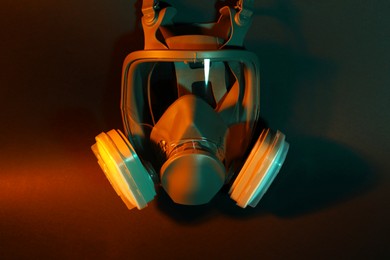 Photo of One respirator mask on dark background in orange light. Safety equipment