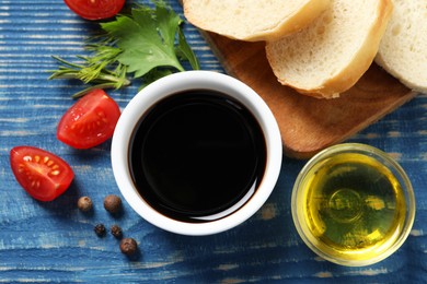 Photo of Balsamic vinegar, bread and other products on blue wooden table, flat lay