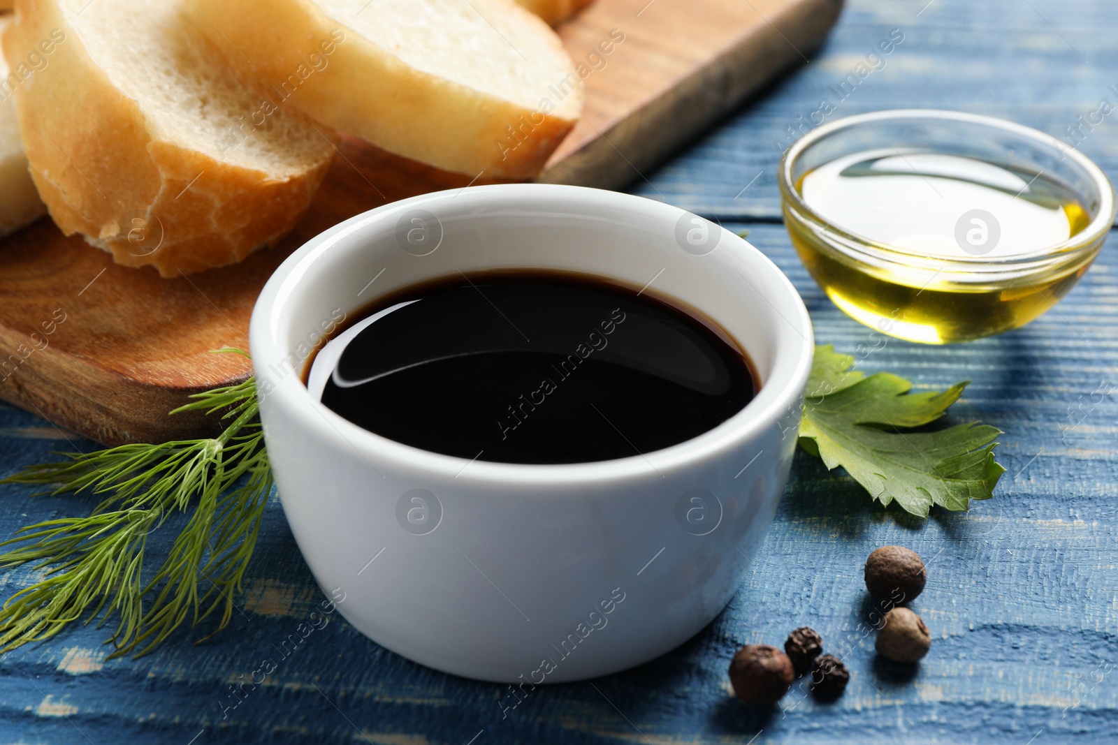 Photo of Balsamic vinegar, bread and other products on blue wooden table, closeup