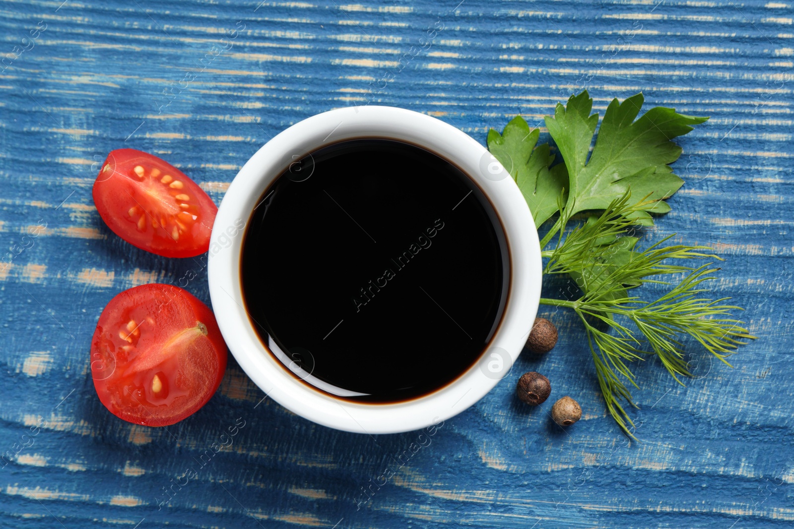 Photo of Balsamic vinegar, tomatoes, peppercorns and herbs on blue wooden table, flat lay