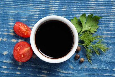 Photo of Balsamic vinegar, tomatoes, peppercorns and herbs on blue wooden table, flat lay