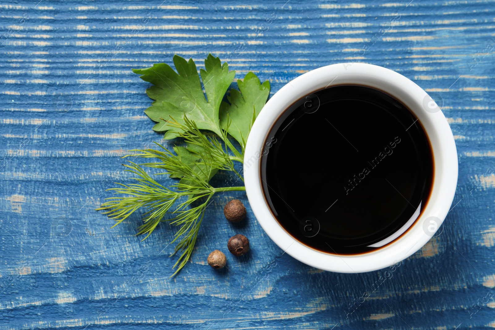 Photo of Balsamic vinegar, parsley, dill and peppercorns on blue wooden table, flat lay