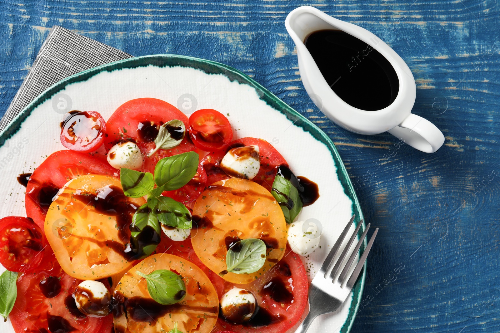 Photo of Tasty salad with balsamic vinegar, mozzarella and fork on blue wooden table, flat lay