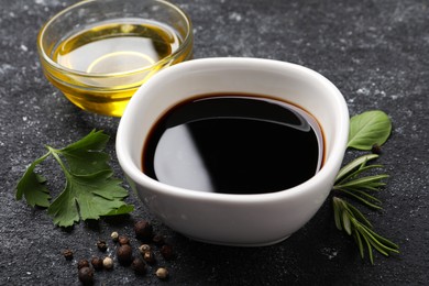 Photo of Balsamic vinegar, oil and other products on black textured table, closeup