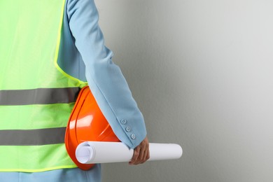 Engineer with hard hat and draft on grey background, closeup. Space for text