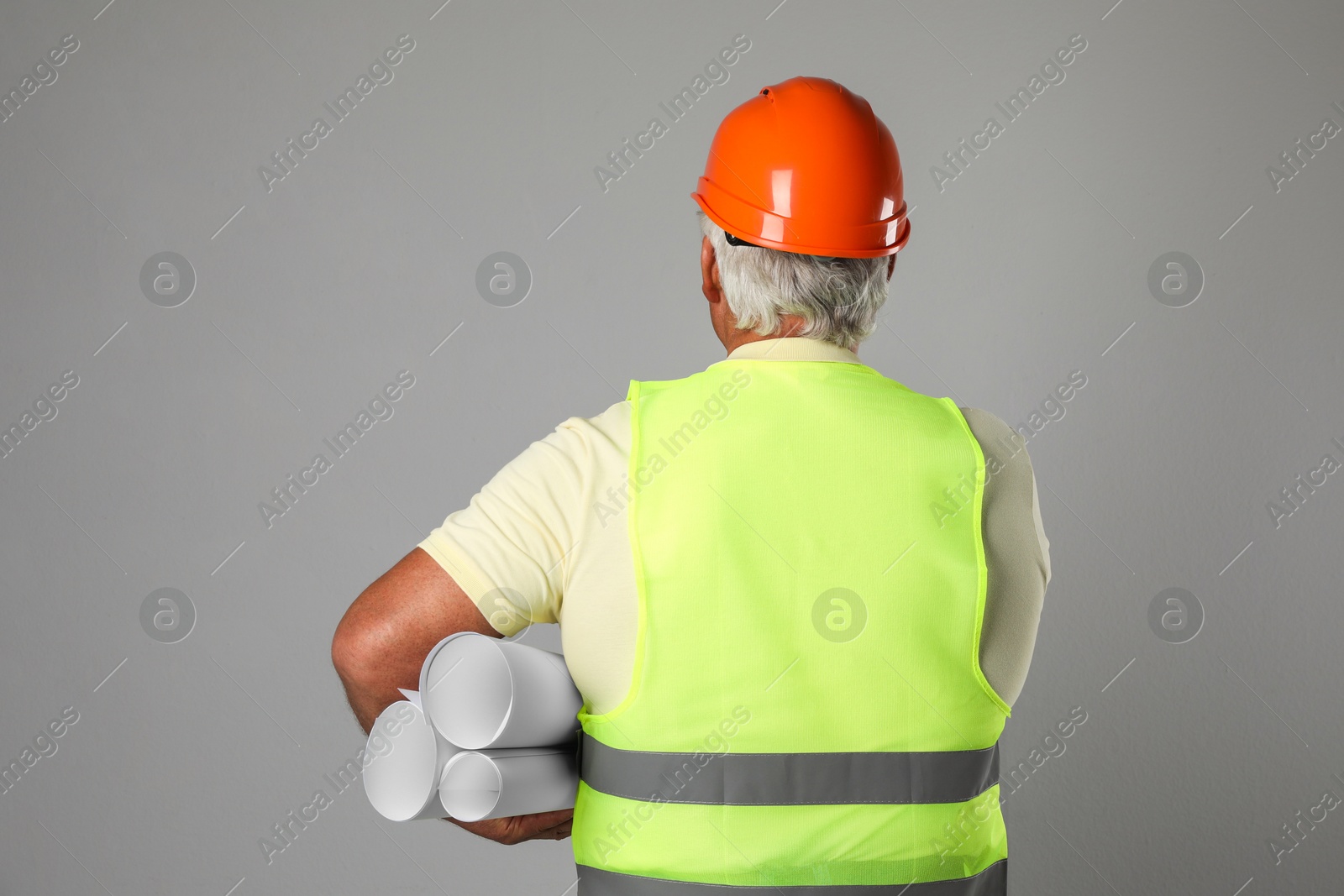 Photo of Engineer in hard hat with drafts on grey background, back view