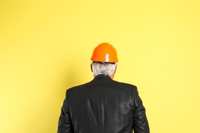 Engineer in hard hat on yellow background, back view