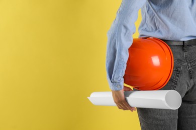 Engineer with hard hat and draft on yellow background, closeup. Space for text