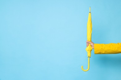 Man holding yellow umbrella on light blue background, space for text