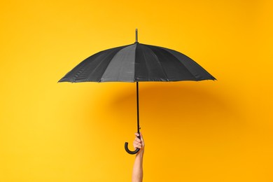 Man holding black umbrella on yellow background, closeup