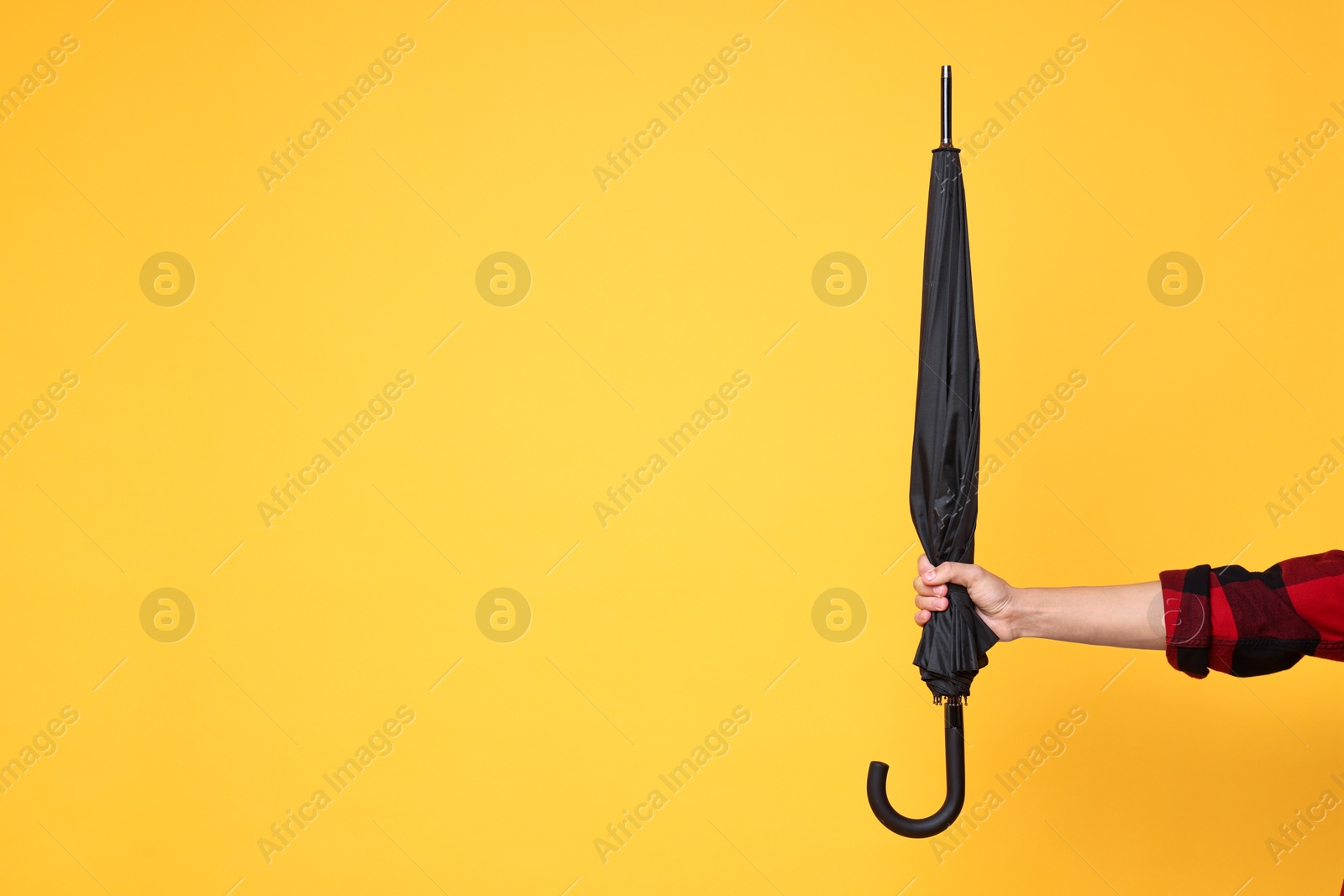 Photo of Man holding black umbrella on yellow background, closeup. Space for text