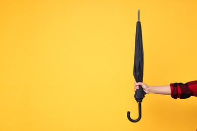 Photo of Man holding black umbrella on yellow background, closeup. Space for text