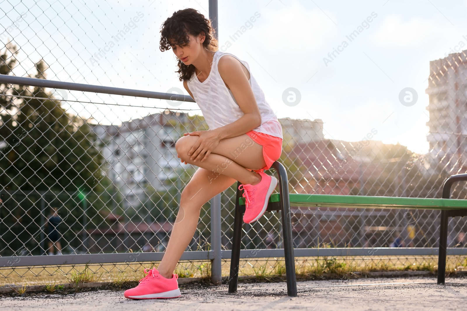 Photo of Sportswoman with leg injury suffering from knee pain near bench at stadium