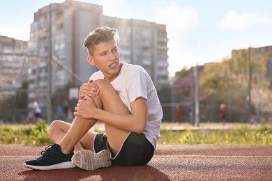 Sportsman with leg injury suffering from knee pain at stadium, space for text