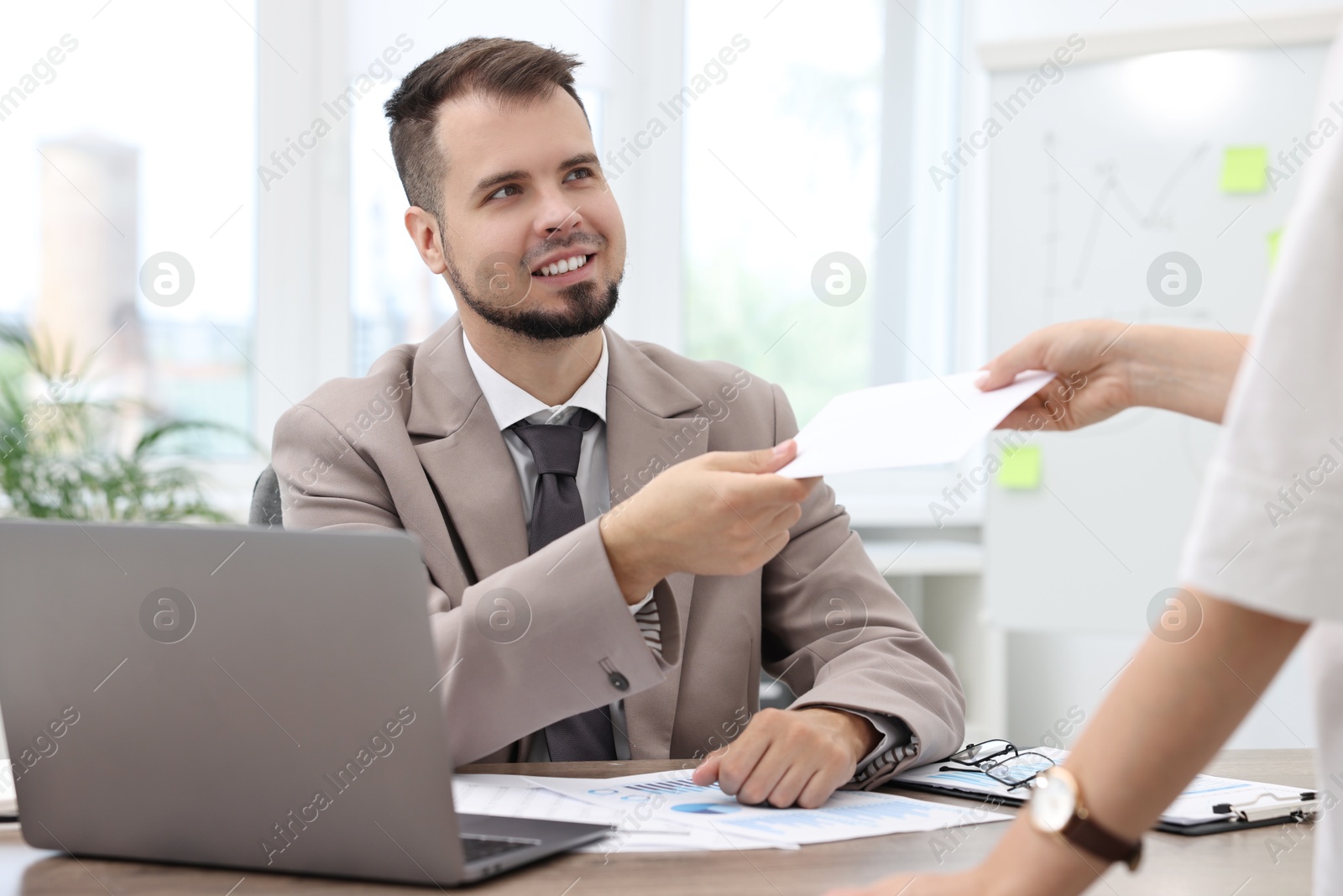 Photo of Smiling employee receiving envelope with salary from boss in office