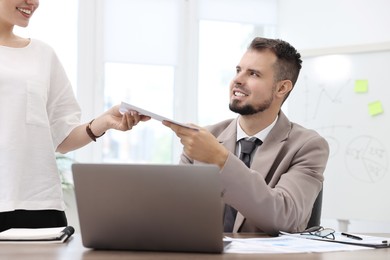 Photo of Smiling employee receiving envelope with salary from boss in office