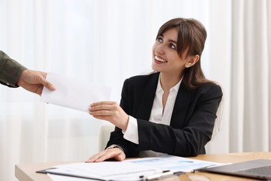 Smiling employee receiving envelope with salary from boss in office