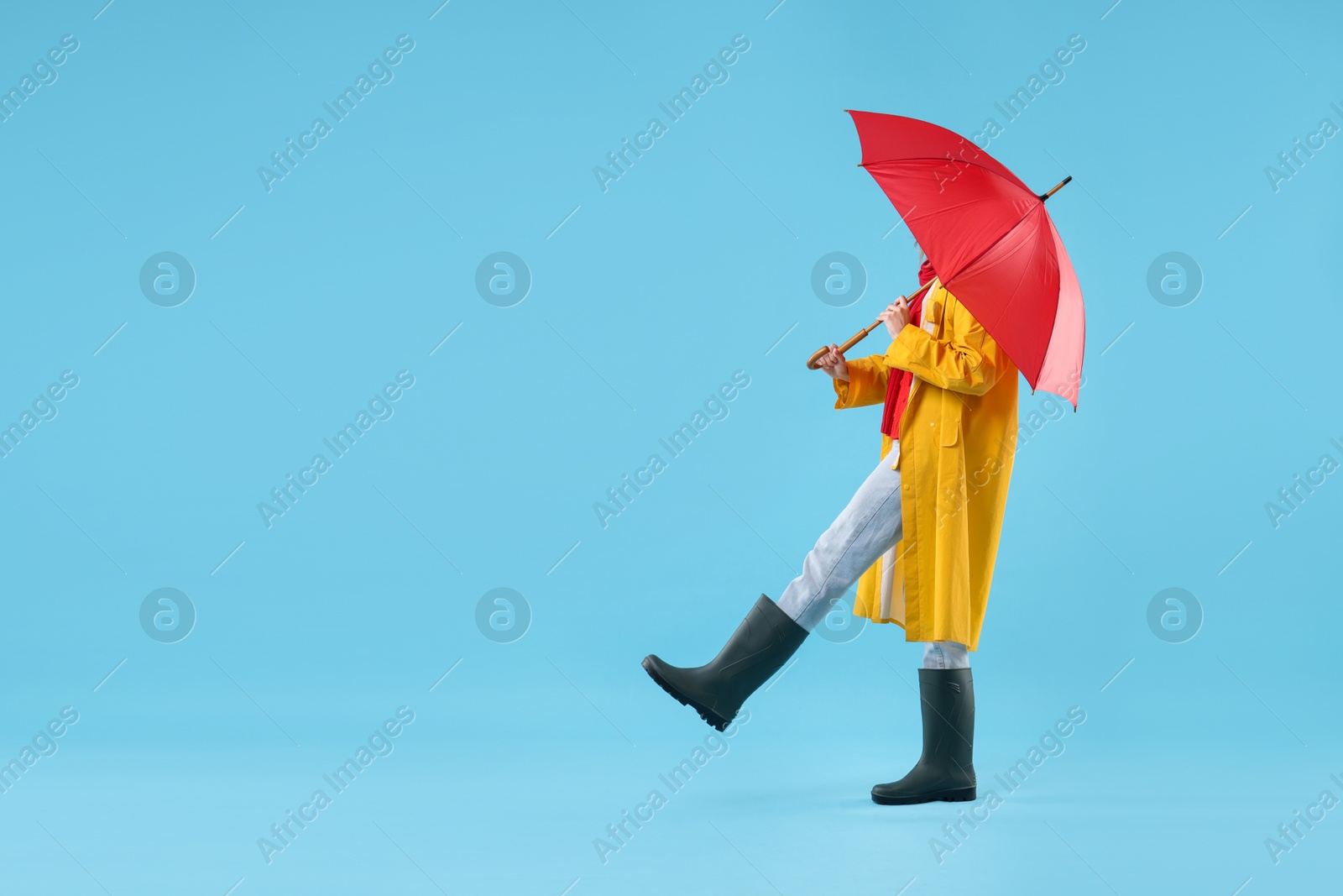 Photo of Woman with red umbrella walking on light blue background, space for text