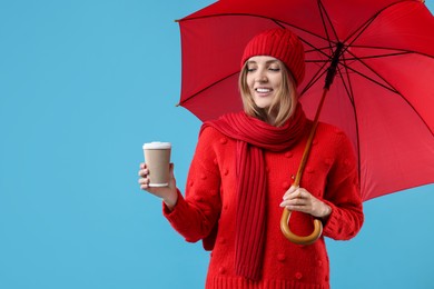 Woman with red umbrella and paper cup on light blue background, space for text