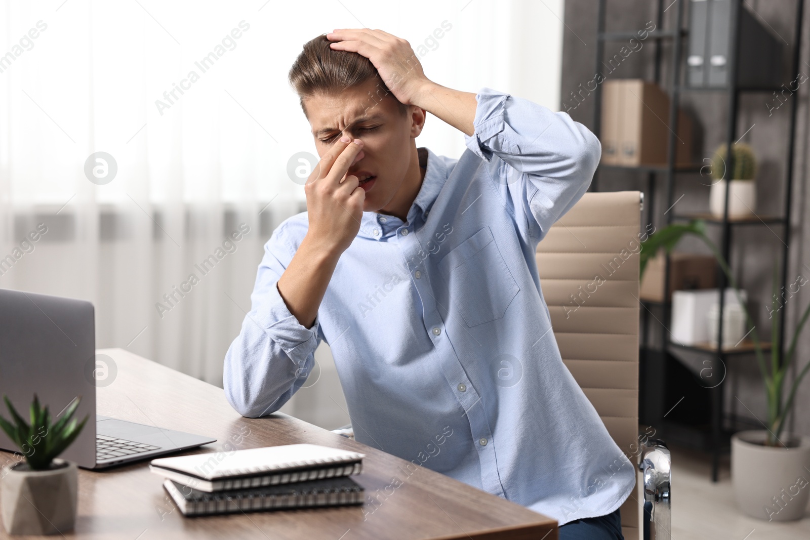 Photo of Young man suffering from sinusitis at wooden table indoors